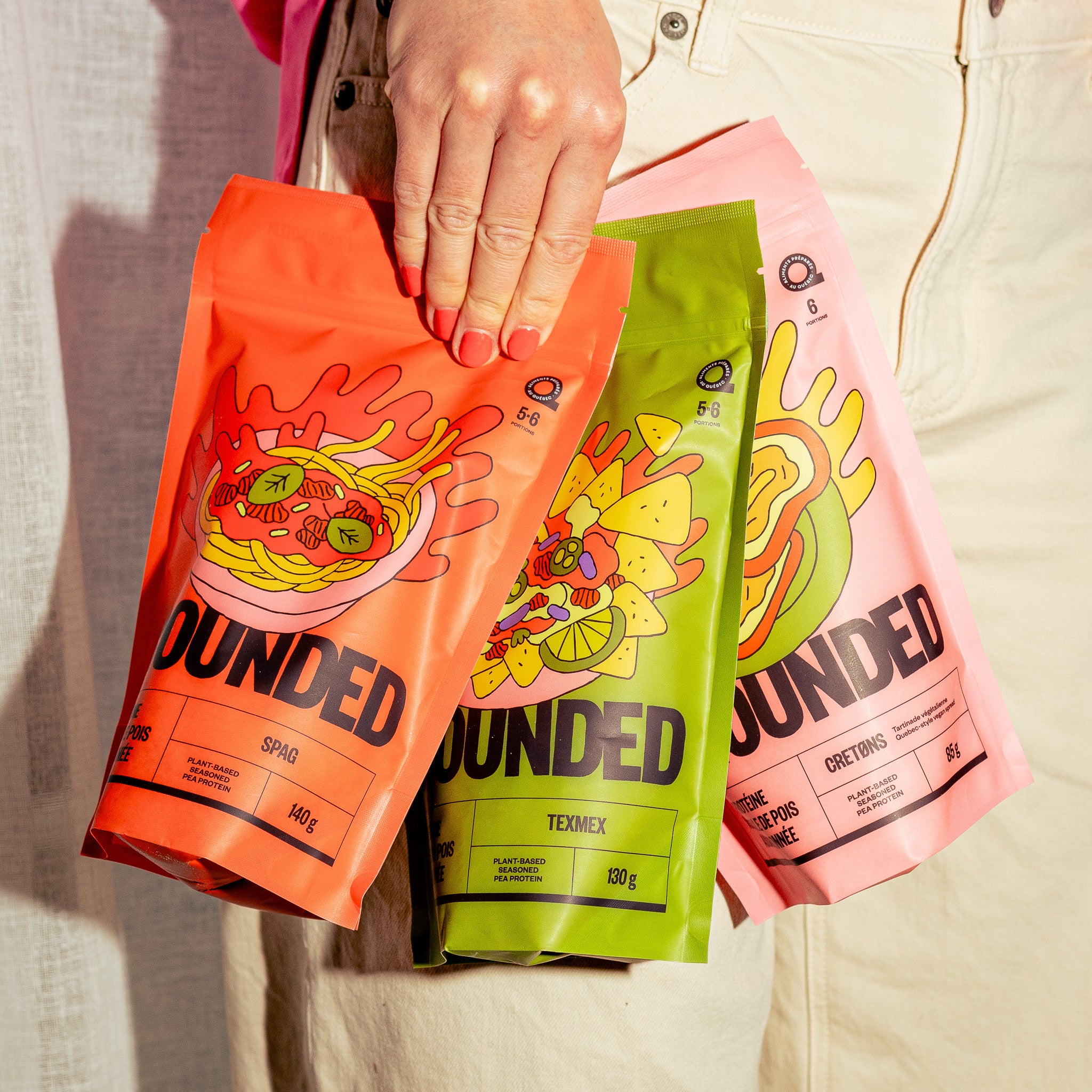 rois sachets Grounded de la boîte découverte tenus à la main représentant les saveurs Spag Texmex et Cretons. Protéines végétales à base de pois jaune dans des emballages colorés pour une alimentation végane pratique et savoureuse.