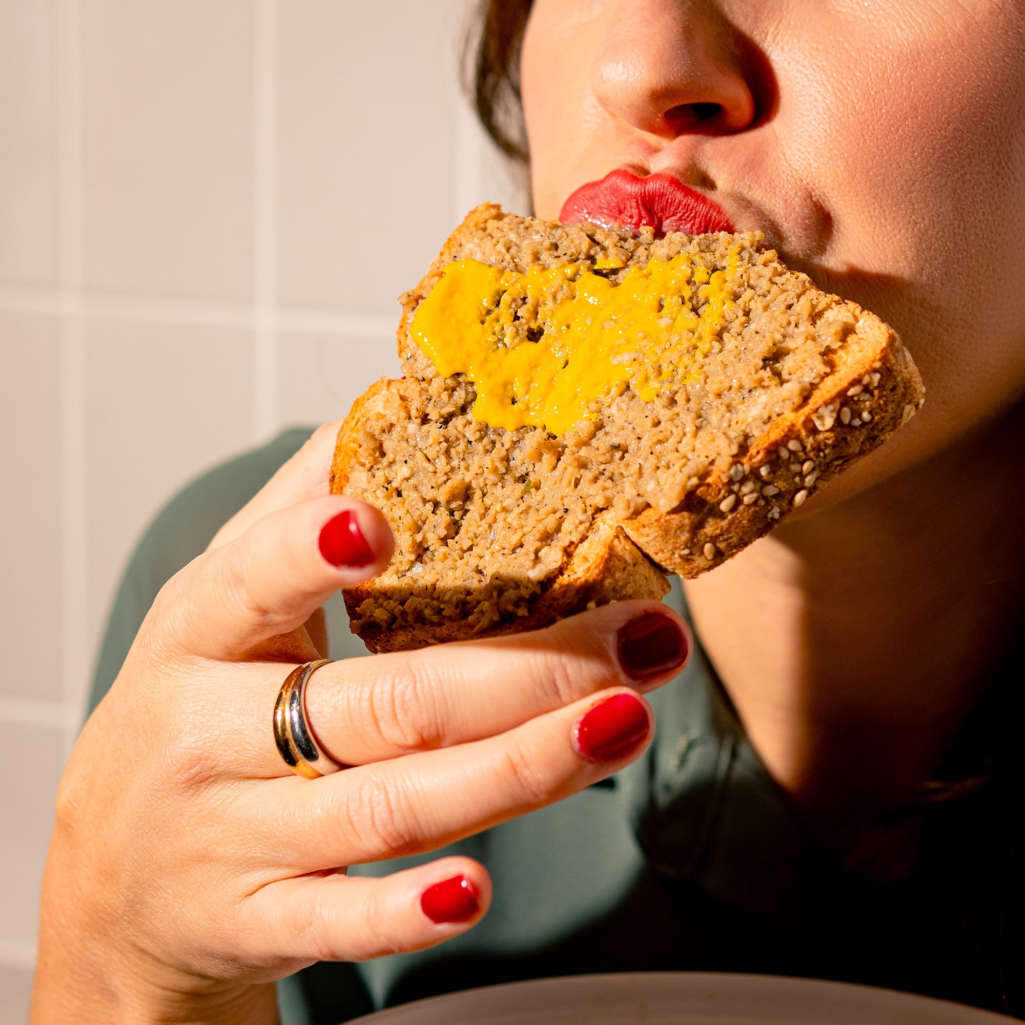 Personne dégustant une tranche de pain garnie de cretons végétaux Grounded avec une touche de moutarde. Tartinade végane à base de protéine de pois jaune.
