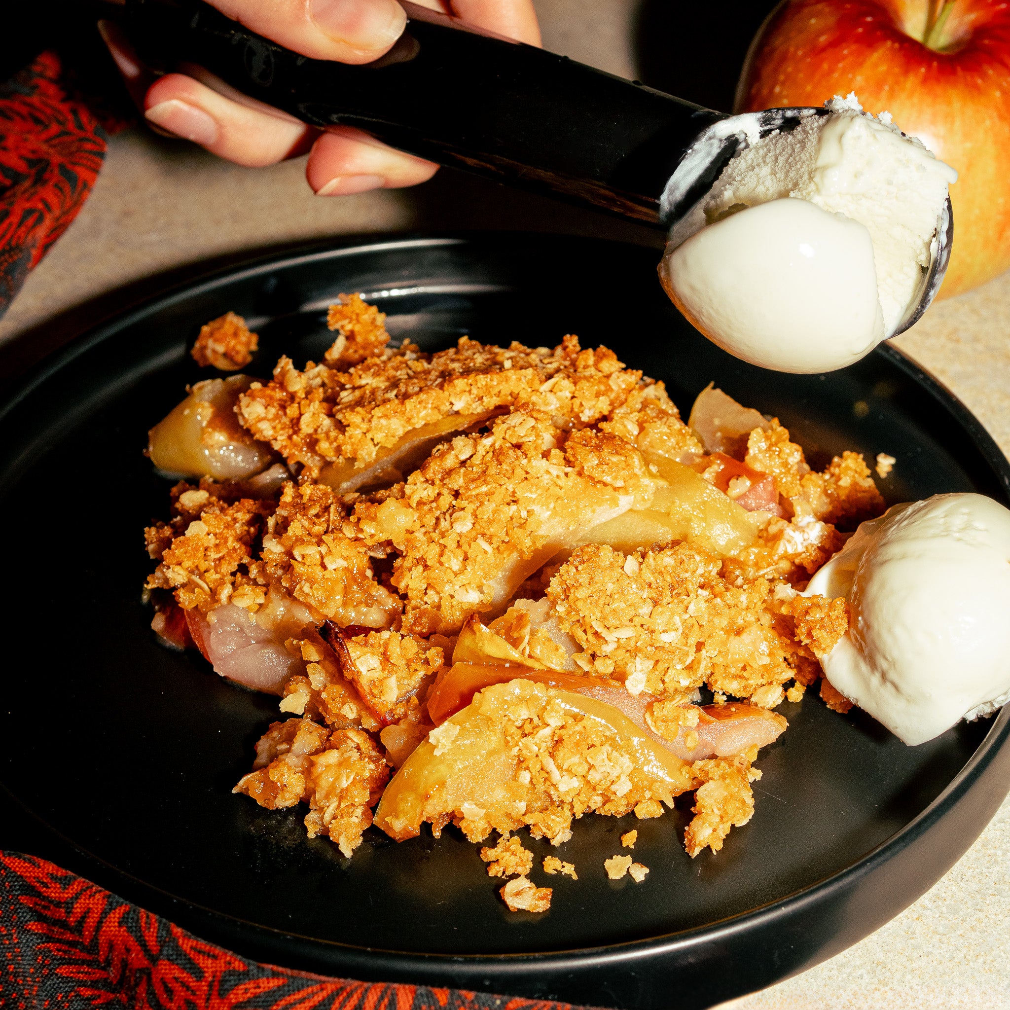 Scène avec une délicieuse croustade aux pommes faite avec la proteine végétale Mini OG GROUNDED. Elle est accompagnée d'une boule de crème glacée à la vanille. Le crumble doré fait avec la PVT Mini OG de grounded apporte de la texture à ce bon dessert.