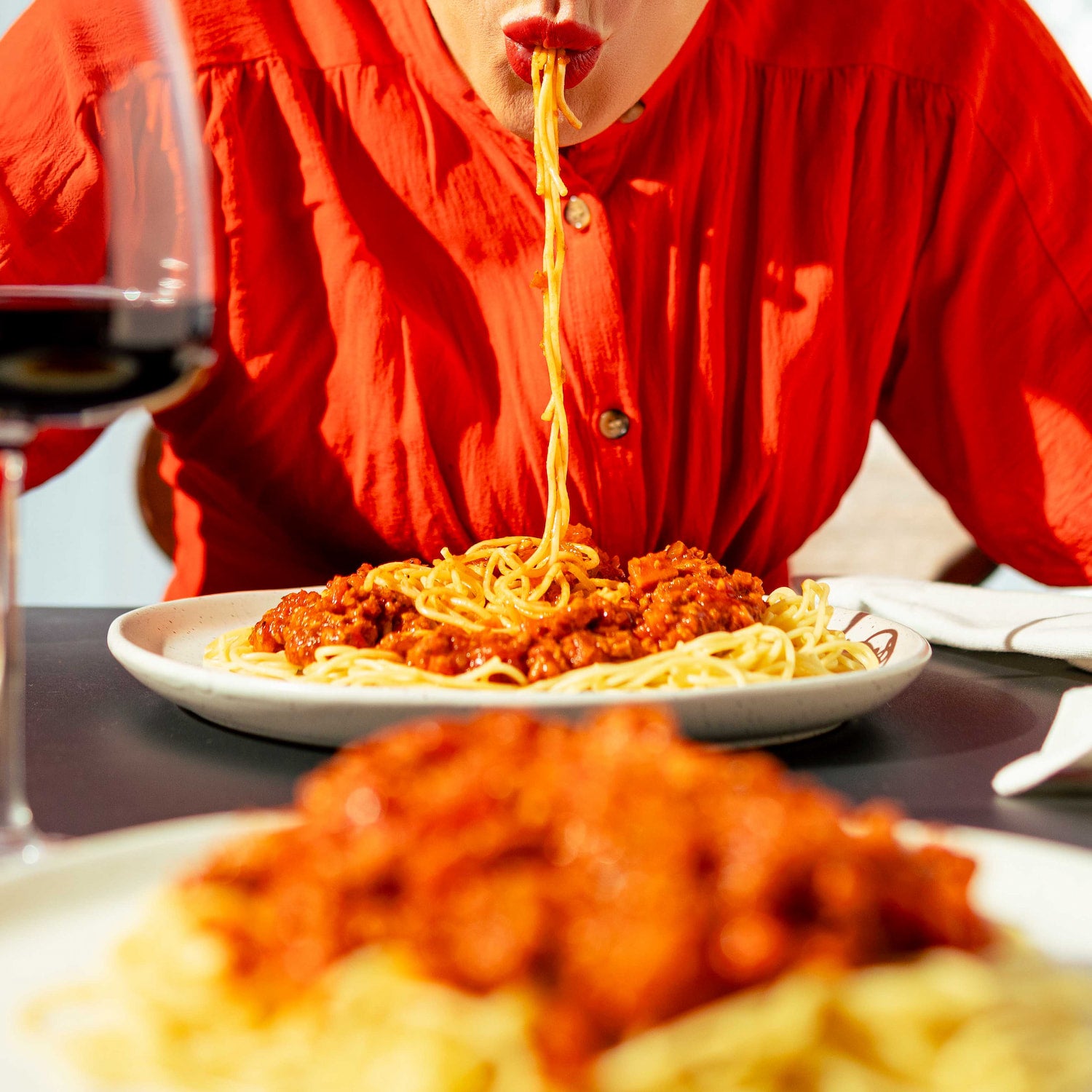 Personne savourant un plat de spaghettis à la sauce bolognaise végétale faite avec une protéine de pois jaunes signée Grounded, accompagnée d’un verre de vin rouge. Scène chaleureuse de repas végétalien gourmand et durable.