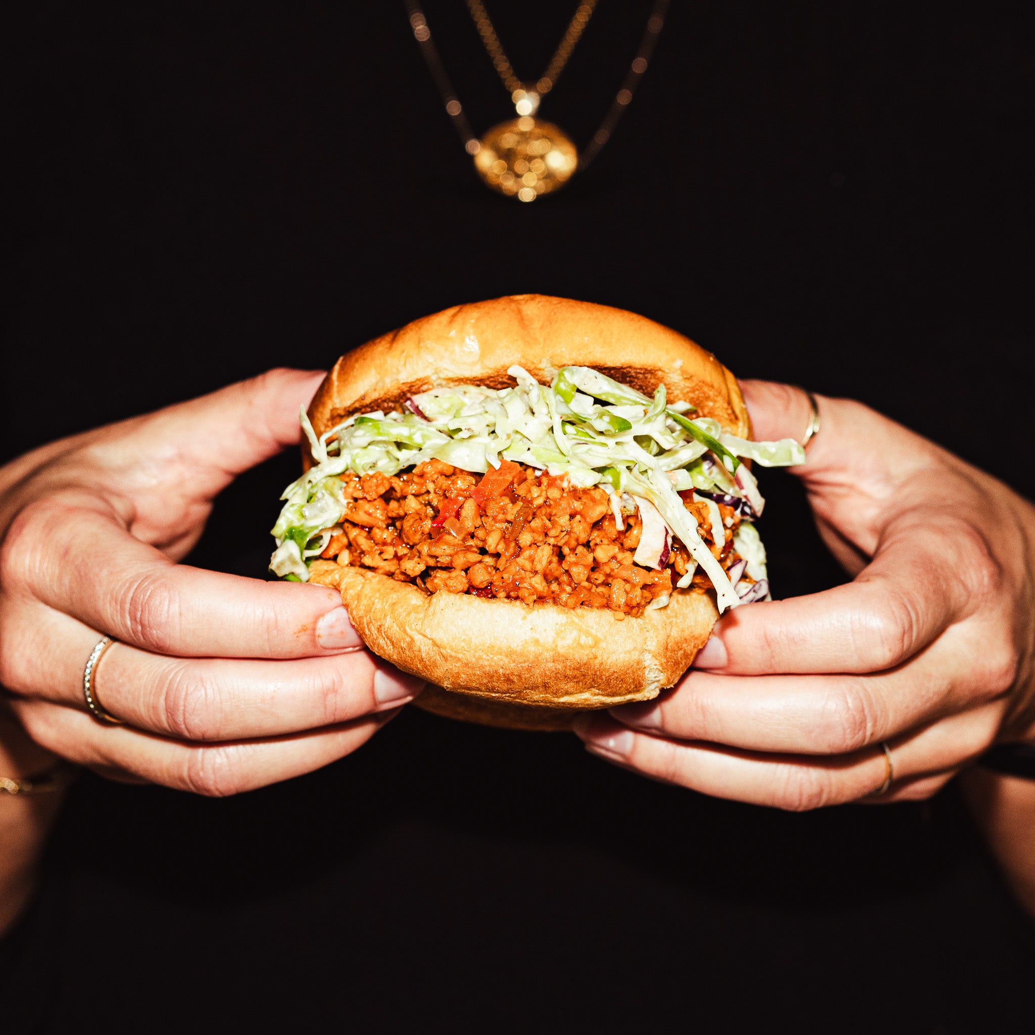 Cette scène représente des mains tenant un sloppy joe réalisé avec la protéine végétale texturée OG GROUNDED. Cette recette est réalisée sans viande, juste avec notre protéine végétale, et délicieuse à souhait.