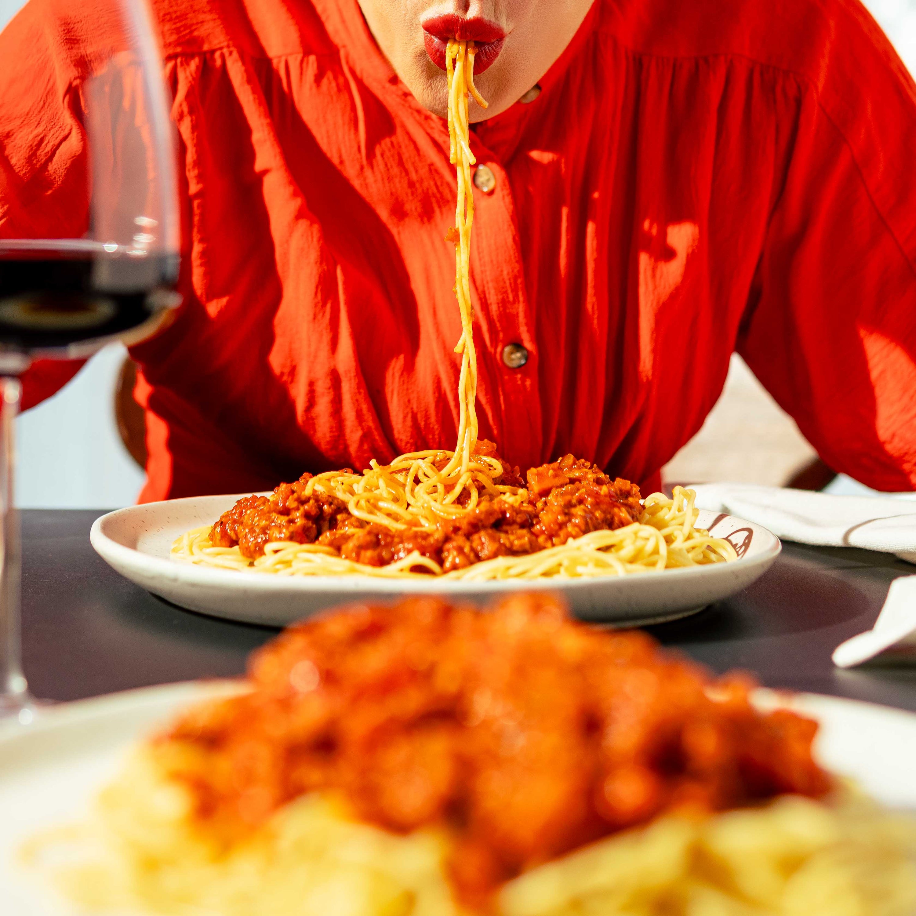 Personne savourant un plat de spaghettis à la sauce bolognaise végétale faite avec une protéine de pois jaunes signée Grounded, accompagnée d’un verre de vin rouge. Scène chaleureuse de repas végétalien gourmand et durable.