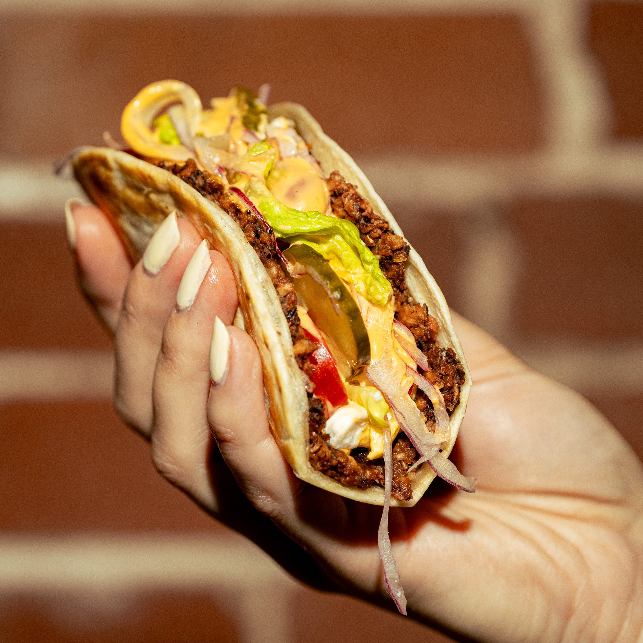 Taco burger végé créé avec Loounie, garni d’une galette de PVT à base de protéines végétales, laitue, cornichons, oignons rouges et sauce gourmande.